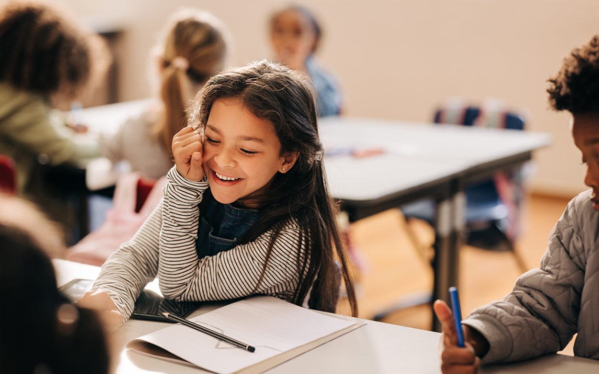 Child sitting in elementary school classroom, smiling