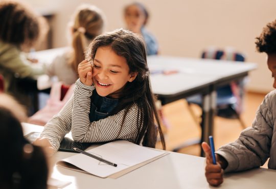 Child sitting in elementary school classroom, smiling