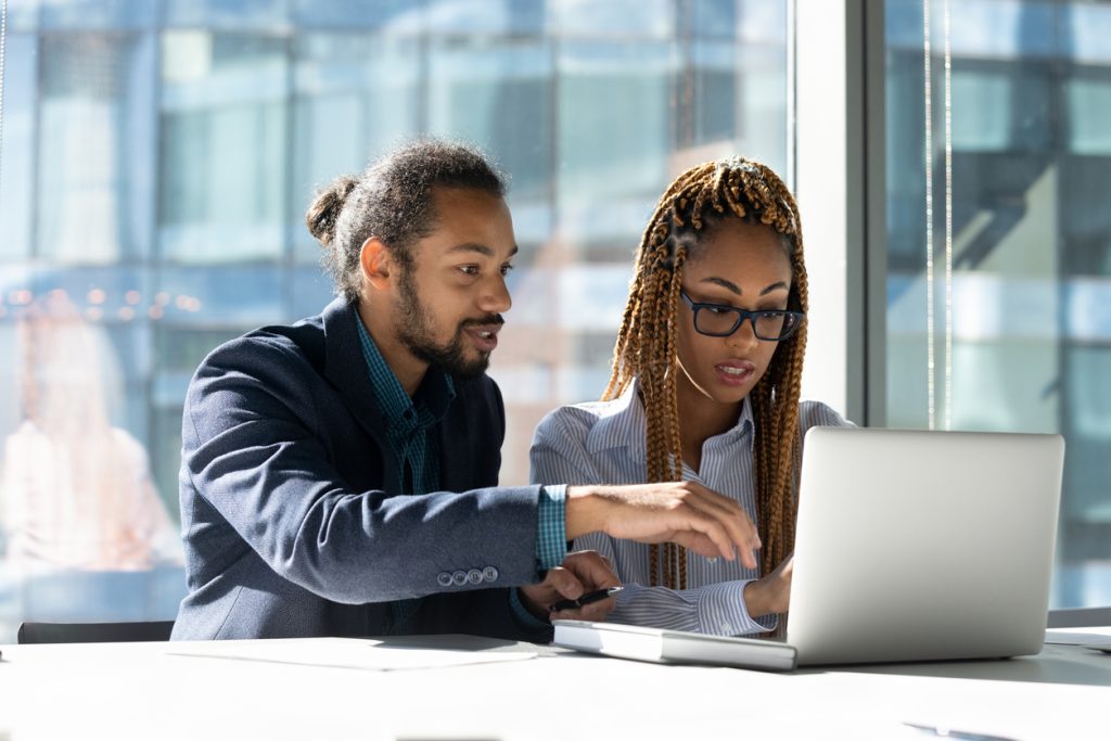 Black man and Black woman sitting looking at computer in office together