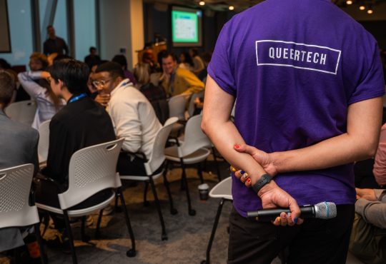 Person wearing purple QueerTech tshirt at conference.