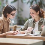 Two people talking in cafe and looking at notebook together