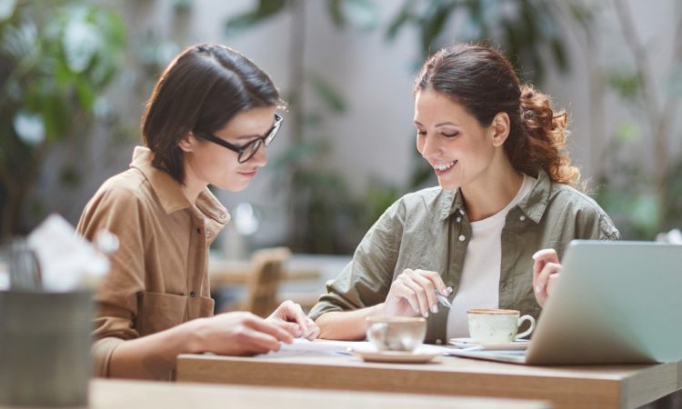 Two people talking in cafe and looking at notebook together