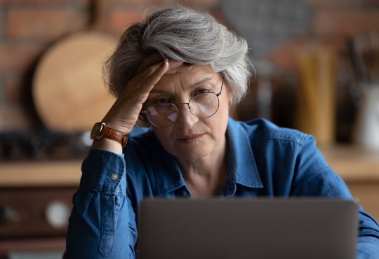 Older woman looking at laptop with their hand on their forehead.