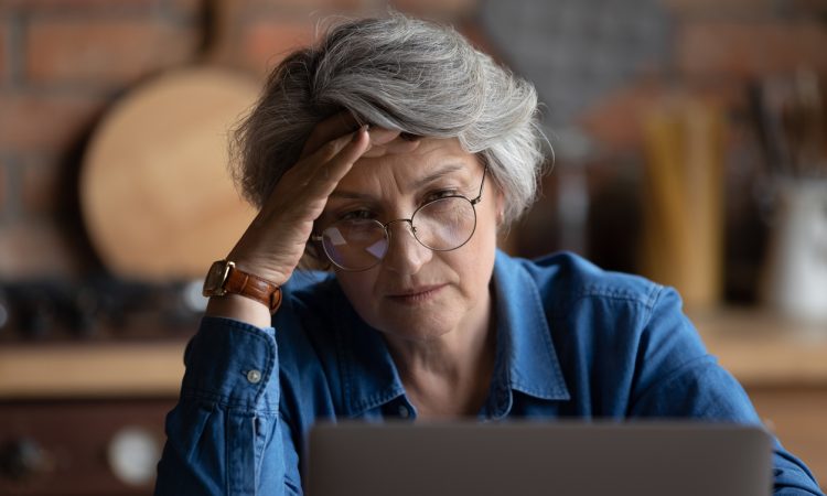 Older woman looking at laptop with their hand on their forehead.