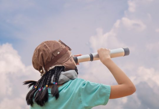 A child looking up at the cloudy sky through a spyglass.