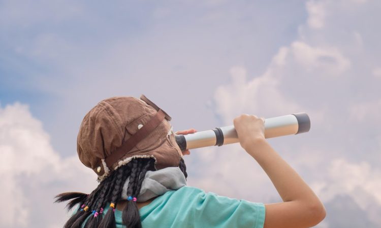 A child looking up at the cloudy sky through a spyglass.