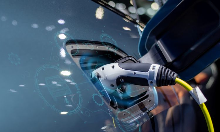 The image shows an electric vehicle charging at a charging station, with a close-up of the charging plug inserted into the vehicle and digital graphics overlaying the scene, suggesting technology and connectivity.