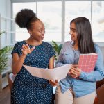 Two women looking at papers together and talking in office