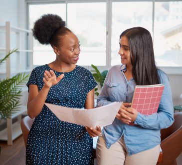 Two women looking at papers together and talking in office