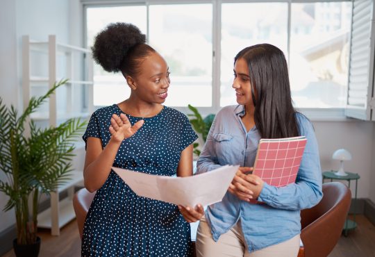 Two women looking at papers together and talking in office