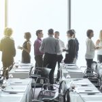 People standing and chatting in a conference room during a break.