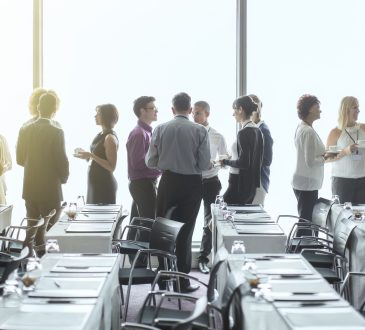 People standing and chatting in a conference room during a break.