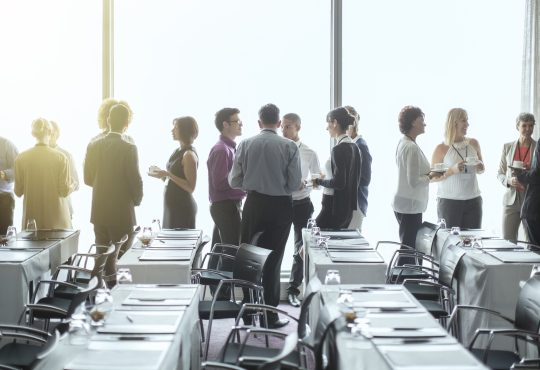 People standing and chatting in a conference room during a break.