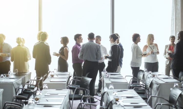 People standing and chatting in a conference room during a break.