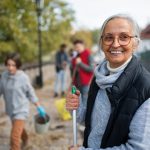 Older woman holding broom outside as part of community clean-up event