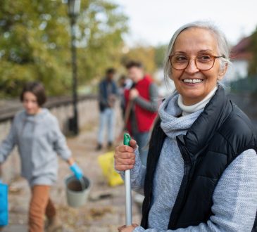 Older woman holding broom outside as part of community clean-up event