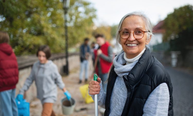 Older woman holding broom outside as part of community clean-up event