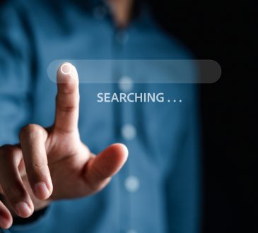 The image shows a person pressing a virtual search icon on a transparent search bar, with the word "SEARCHING..." displayed.