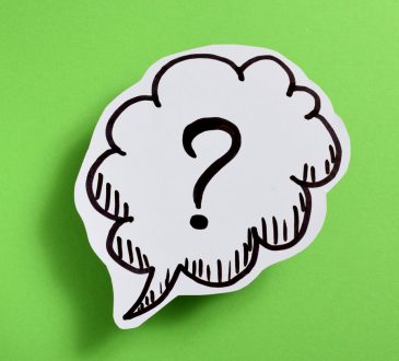 Paper cut-out with a speech bubble and question mark in it on-top of a green background.