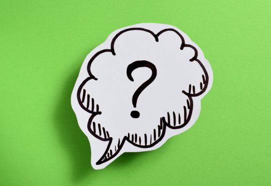 Paper cut-out with a speech bubble and question mark in it on-top of a green background.