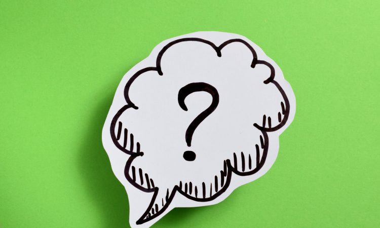 Paper cut-out with a speech bubble and question mark in it on-top of a green background.