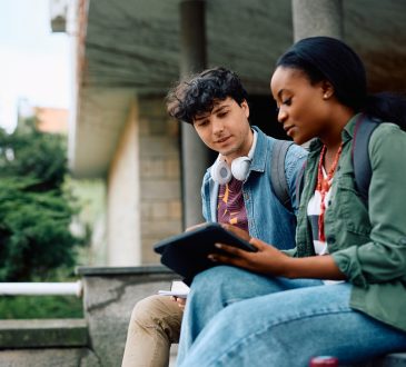 Two college students sitting outside looking at tablet together.