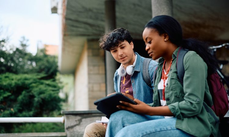 Two college students sitting outside looking at tablet together.