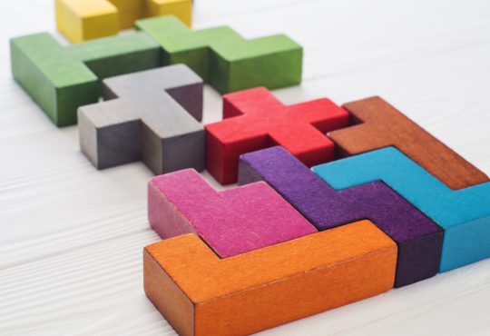 The image shows colorful 3D puzzle pieces resembling Tetris blocks arranged on a white surface.