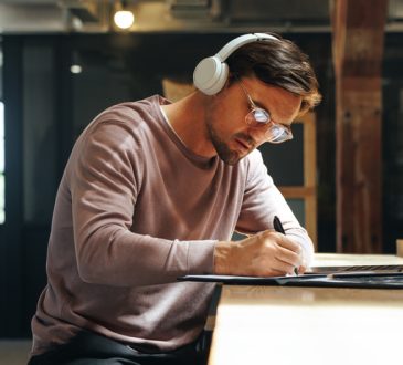 Man sitting at high table writing and wearing over-ear headphones