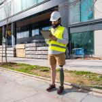 Engineer with prosthetic leg working on construction site wearing protective equipment
