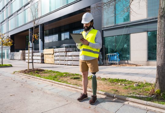 Engineer with prosthetic leg working on construction site wearing protective equipment