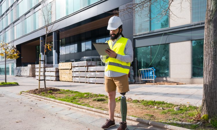 Engineer with prosthetic leg working on construction site wearing protective equipment