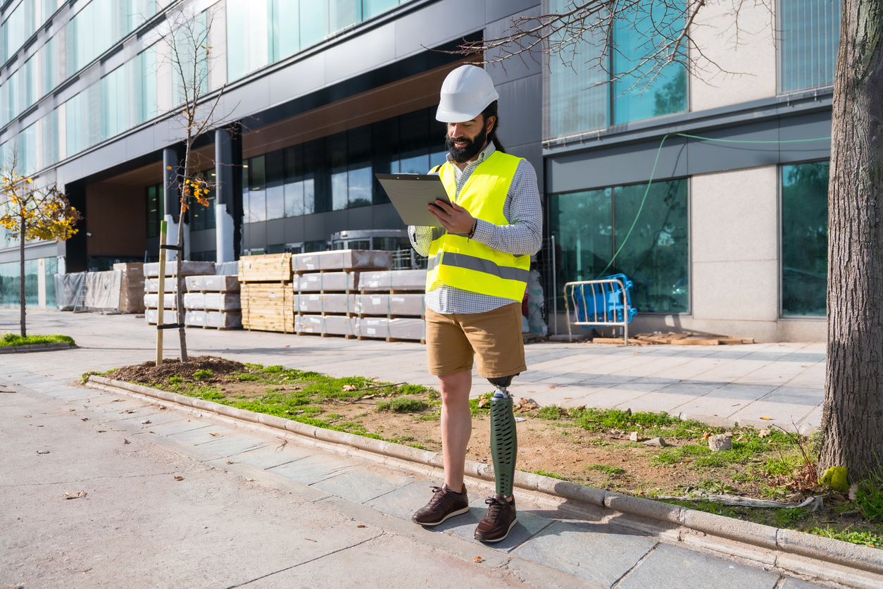 Engineer with prosthetic leg working on construction site wearing protective equipment