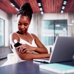 Woman sitting at desk checking glucose monitor on arm