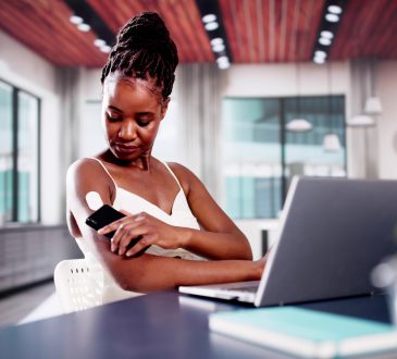 Woman sitting at desk checking glucose monitor on arm