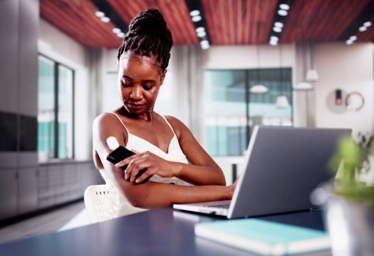 Woman sitting at desk checking glucose monitor on arm