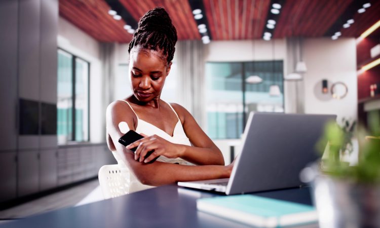 Woman sitting at desk checking glucose monitor on arm