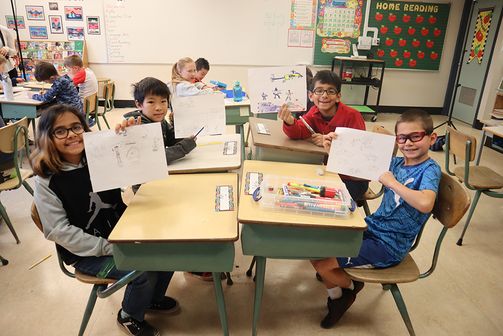 Students hold up their illustrations in a classroom. 