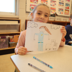 Young girl holding up drawing in classroom.