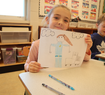 Young girl holding up drawing in classroom.