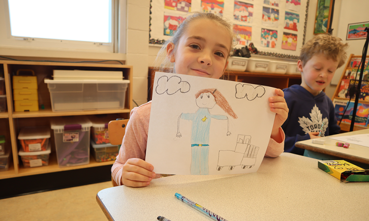 Young girl holding up drawing in classroom.