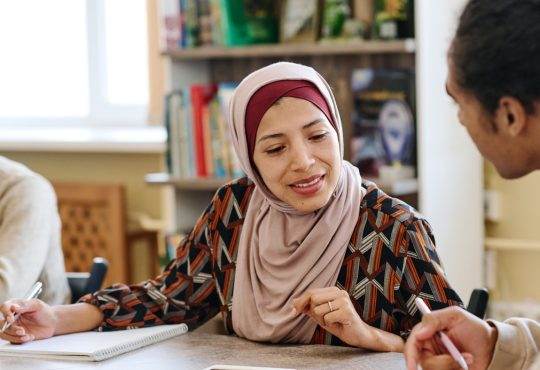 Muslim woman wearing hijab sitting at table in library