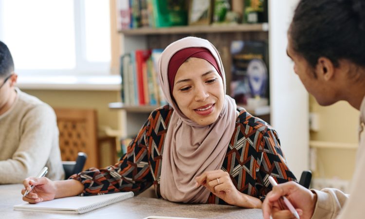 Muslim woman wearing hijab sitting at table in library