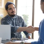 Two people shaking hands across desk in office