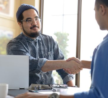 Two people shaking hands across desk in office