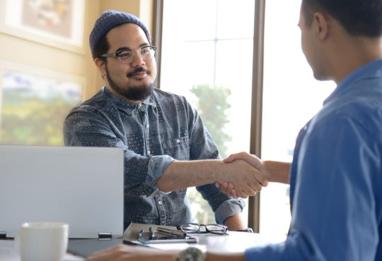 Two people shaking hands across desk in office