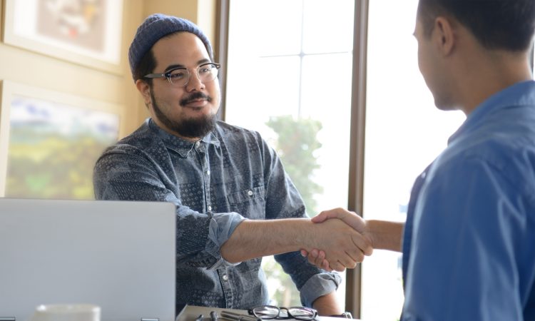 Two people shaking hands across desk in office