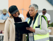 Person wearing safety vest talking to volunteer at food sort