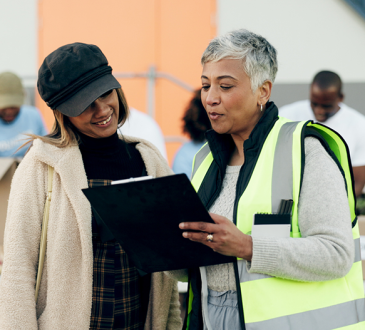 Person wearing safety vest talking to volunteer at food sort