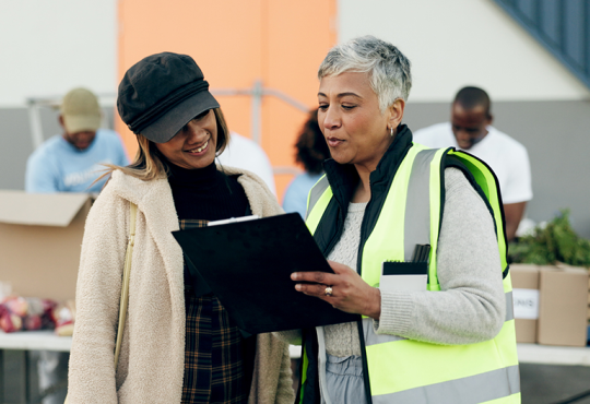 Person wearing safety vest talking to volunteer at food sort